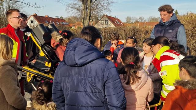 Die DRK-Sanis Valentin Busse und Carolina Kirscht erklärten ausführlich alles rund um die Funktionsweise der Trage aus dem Rettungswagen. | Foto: Caritas